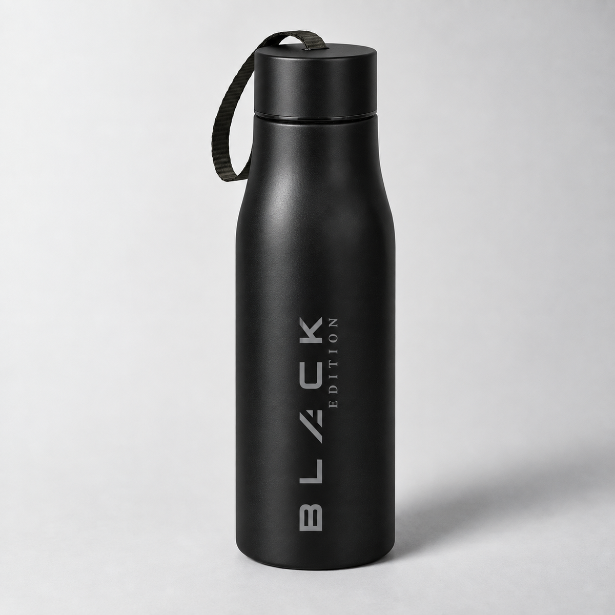 The Black Edition stainless bottle in matte black, with screw cap and woven carry strap, engraved wordmark running vertically up the body.