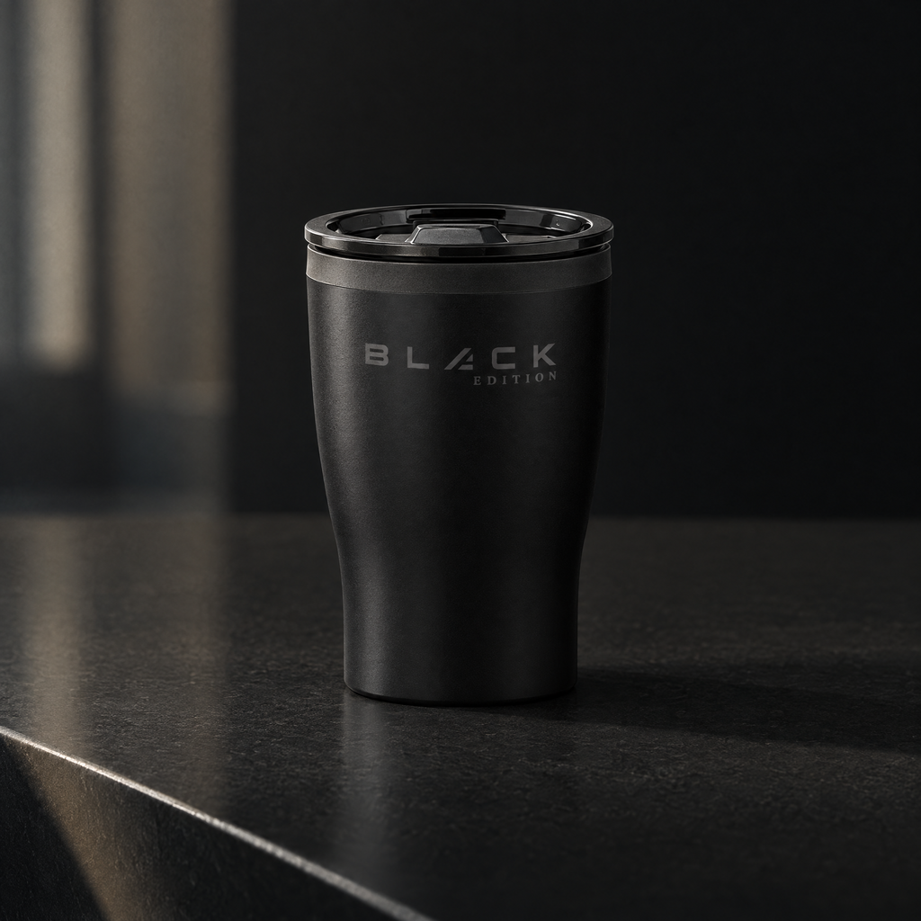 The Black Edition travel cup in matte black with the slider lid fitted, on a dark stone benchtop in morning light, engraved wordmark facing the camera.